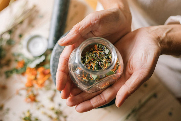 Hands holding a glass jar of dried botanicals