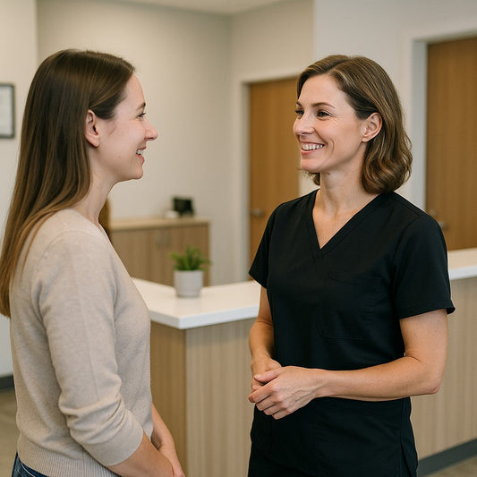 Female chiropractor in stylish black scrubs smiling and advising a patient at the reception desk of a modern clinic, captured from a side angle.