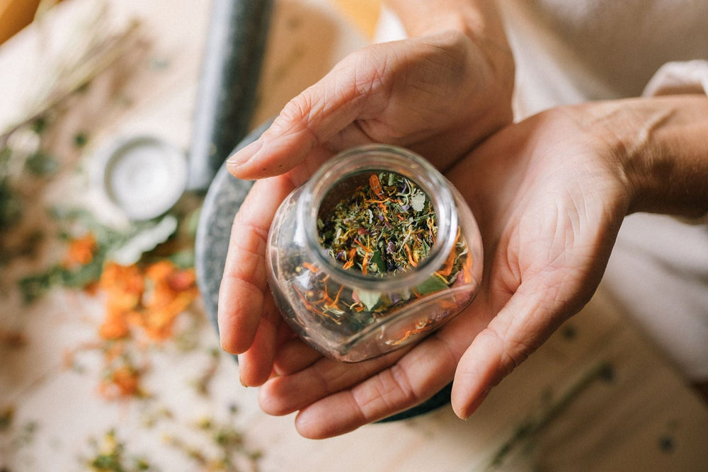 Hands holding a glass jar of dried botanicals