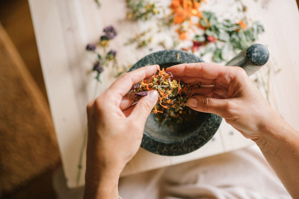 Hands mixing herbs and flowers in a stone mortar